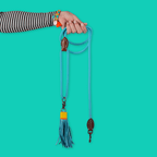 Hand holding a blue lanyard with tassels against a teal background